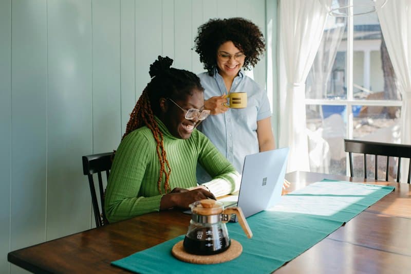 Duas mulheres sorrindo enquanto planejam no notebook, na mesa de casa